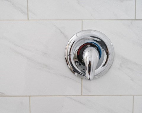 A chrome faucet on a white marble wall.