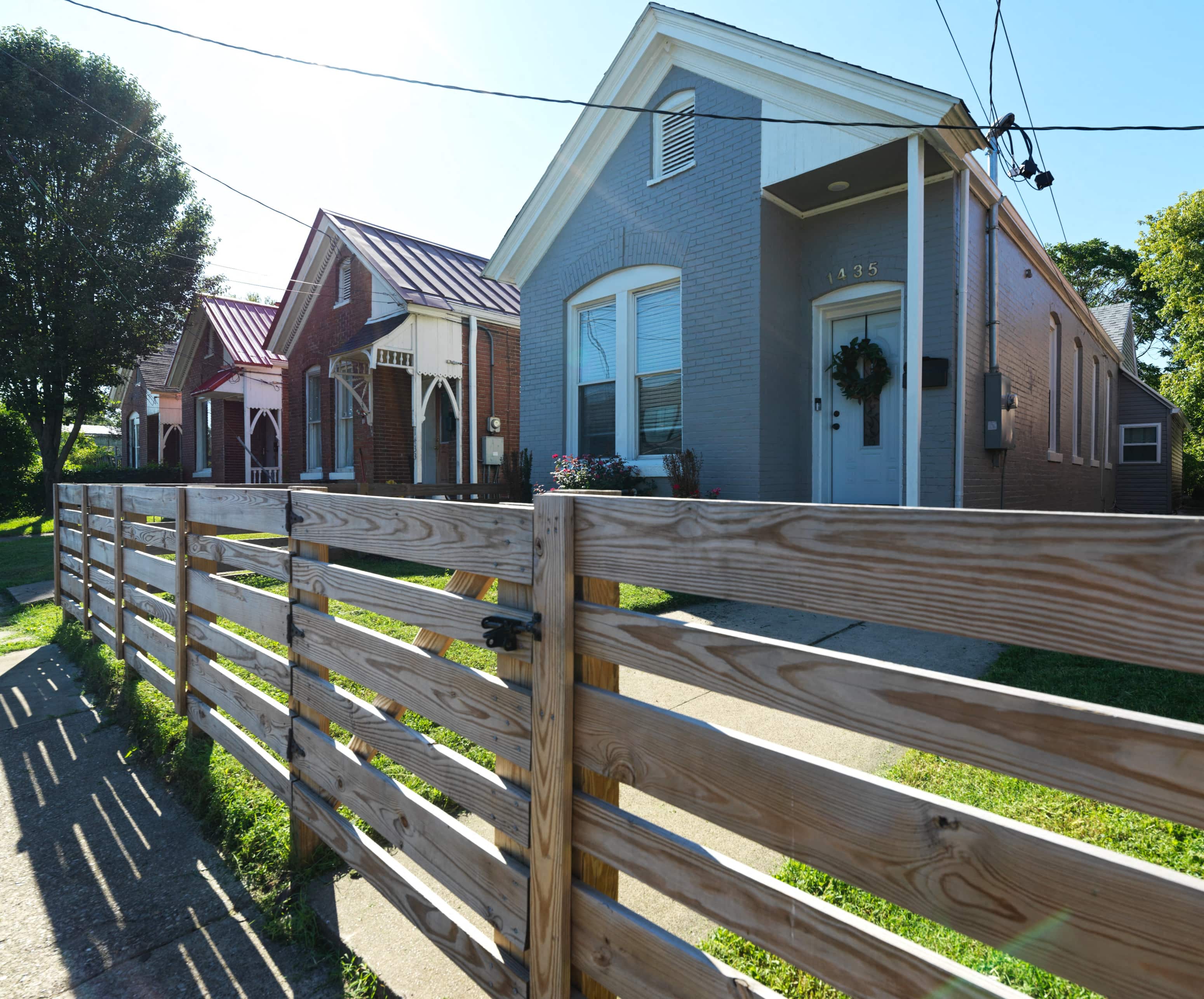 A wooden fence in front of a grey house with a wreath on the door.