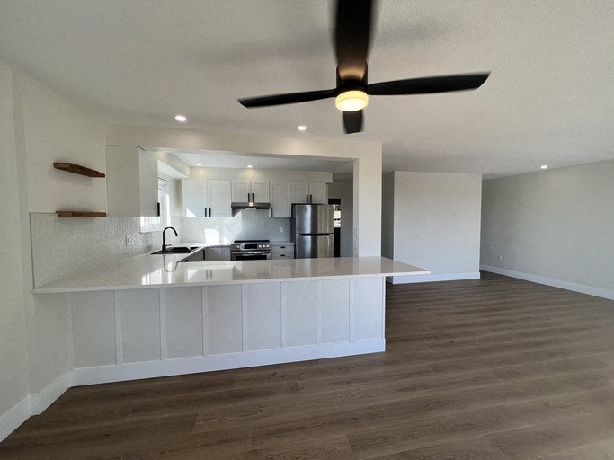 an empty living room with a kitchen and a ceiling fan