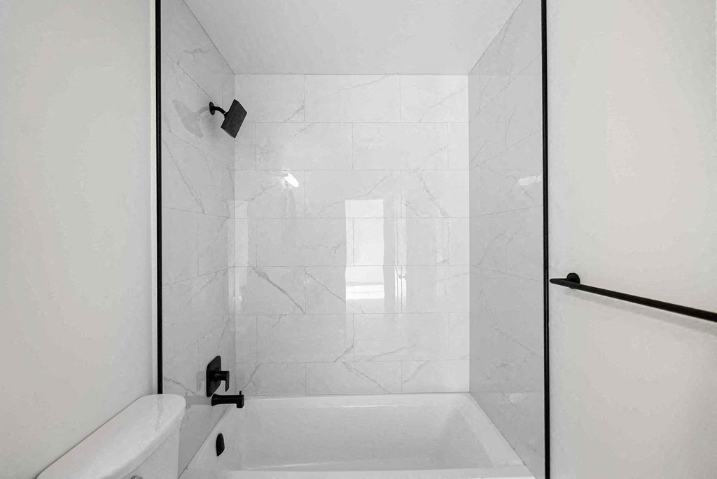the bathroom is tiled in white marble and has a shower and tub