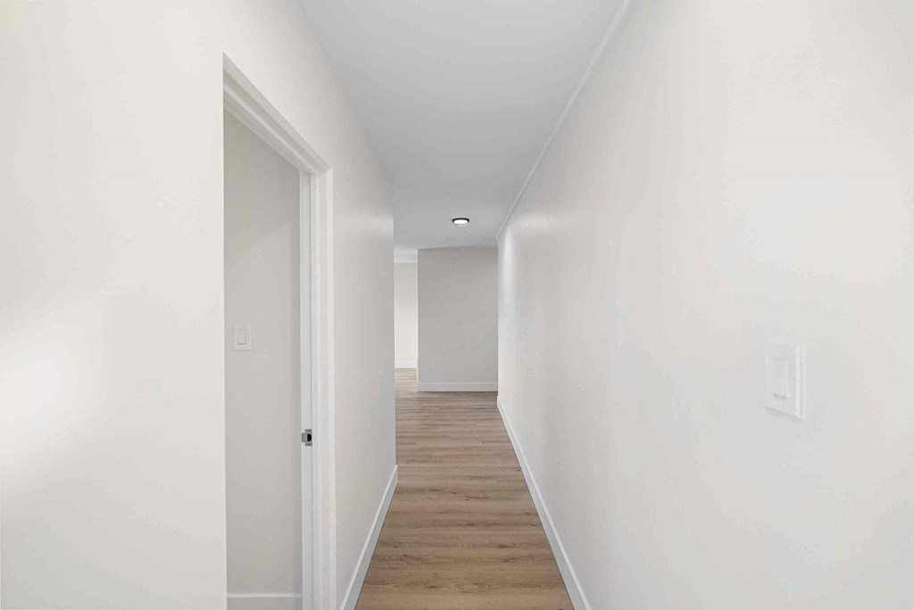 a hallway with white walls and wood floors and a white door