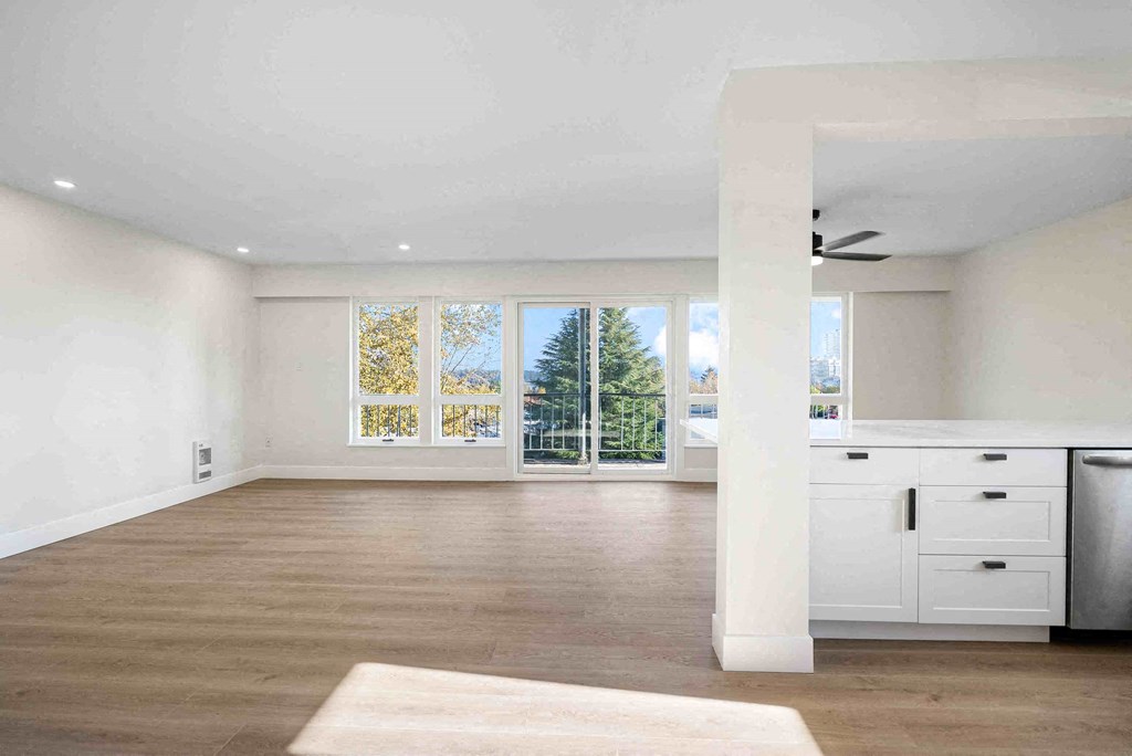 an empty living room with a kitchen and a window