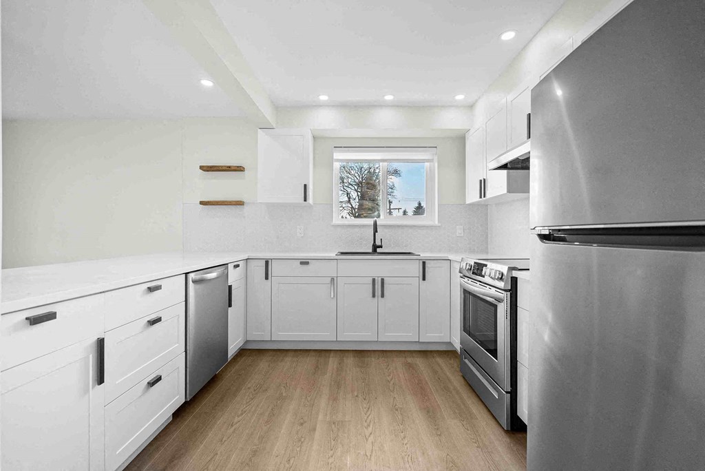 a white kitchen with stainless steel appliances and a window