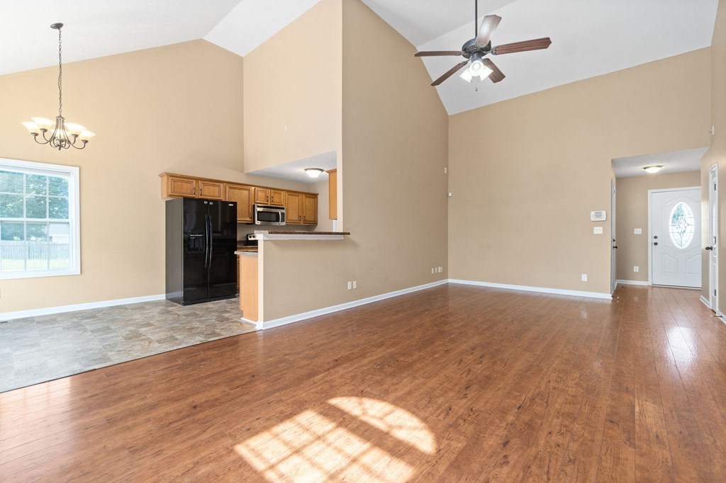 an empty living room with a ceiling fan and a kitchen