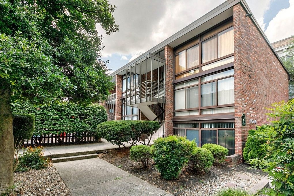 A modern building with a red brick facade and large windows is surrounded by a well-manicured garden.