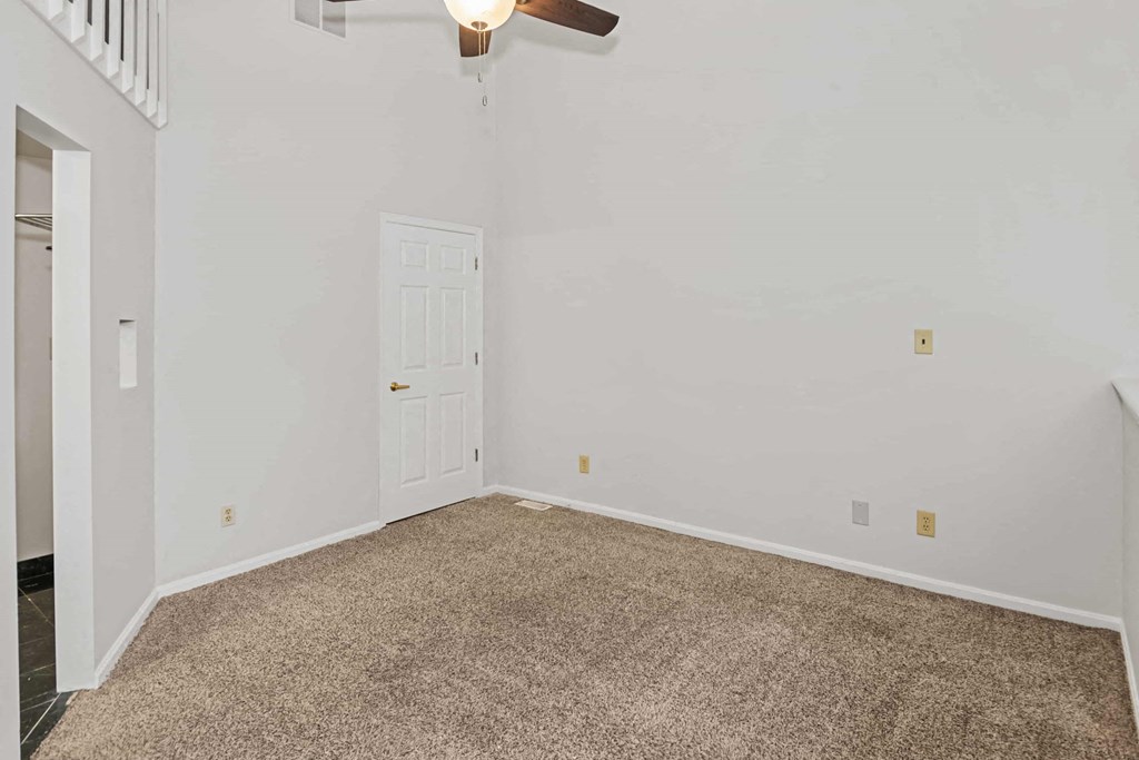 A room with a carpeted floor and a ceiling fan.