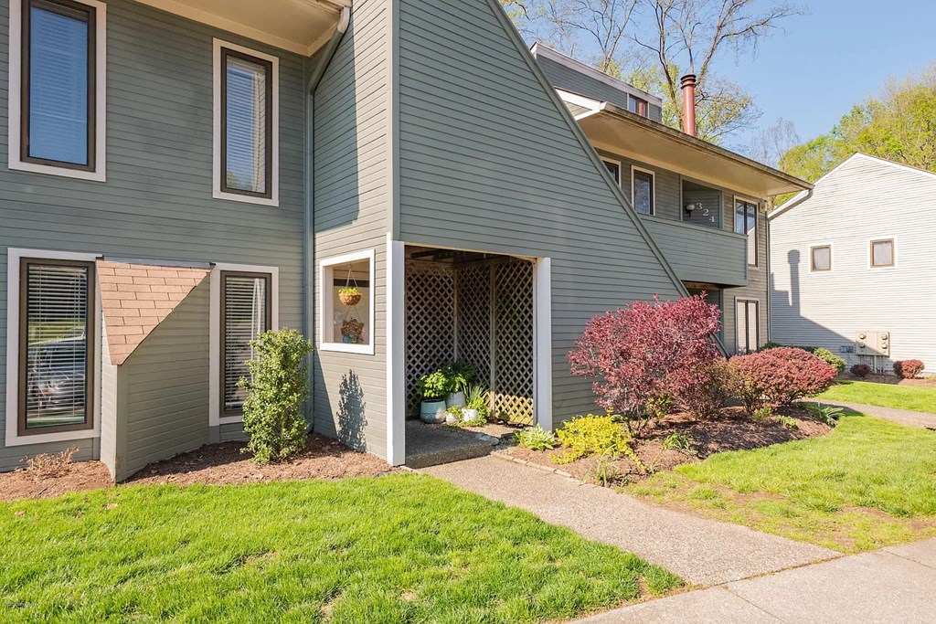 A house with a grey siding and a red bush in front.