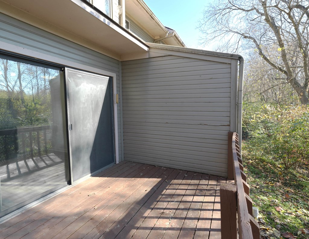 A wooden deck with a sliding glass door leading to a backyard.