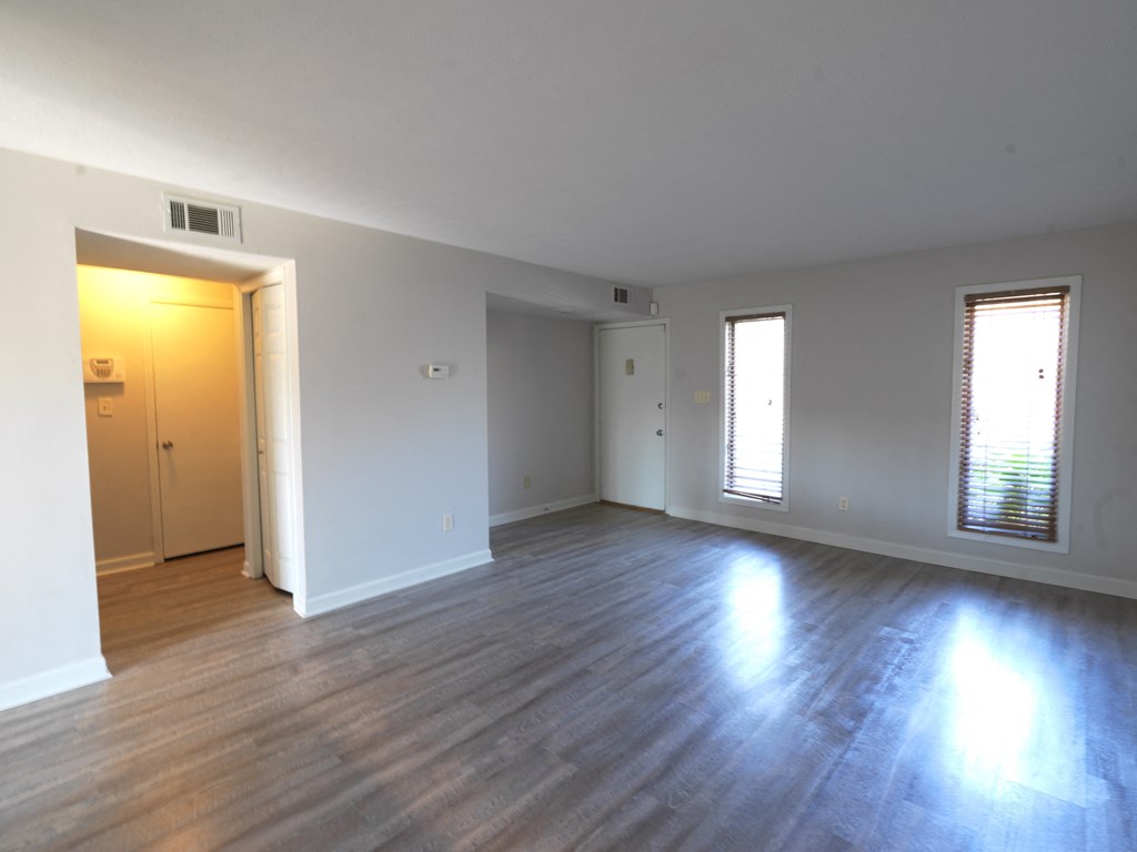 A room with wooden floors and two windows with blinds.