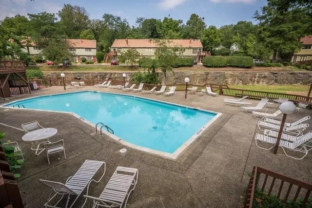 A swimming pool surrounded by chairs and trees.