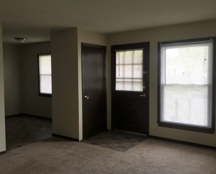 an empty living room with a door and two windows