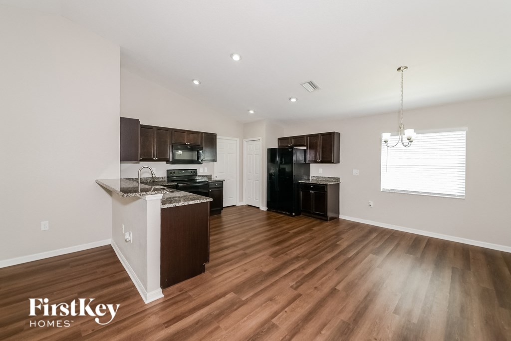 the living room and kitchen of an apartment with wood flooring and black appliances