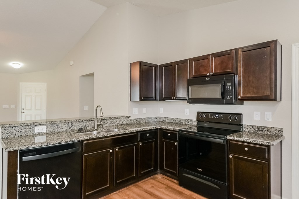 a kitchen with dark wood cabinets and granite counter tops and black appliances