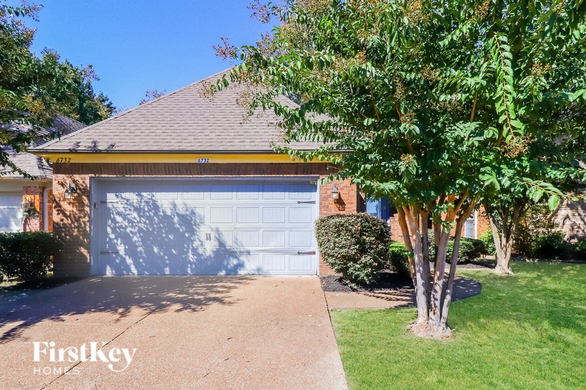 A house with a garage door and a tree in front.