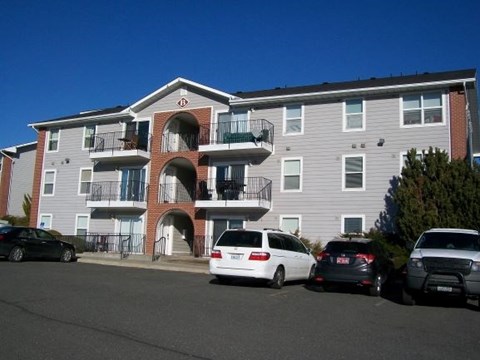 A white car is parked in front of a grey apartment building.