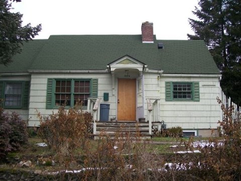A white house with a green roof and a brown door.