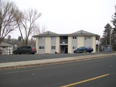 A two-story building with a garage door is situated on a street with a parked car and a van.