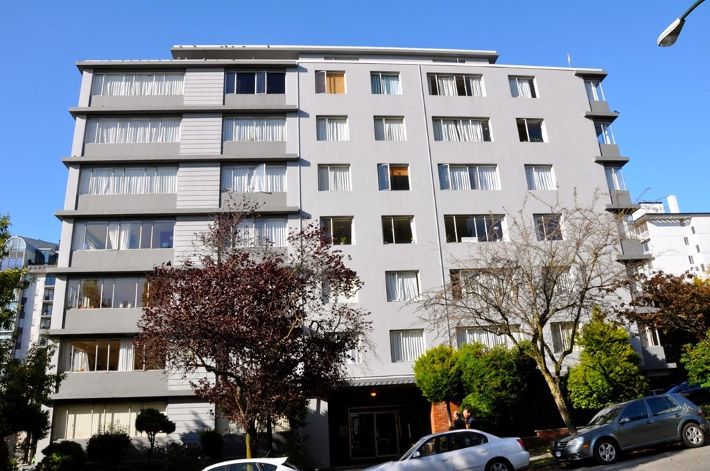A grey apartment building with cars parked in front.