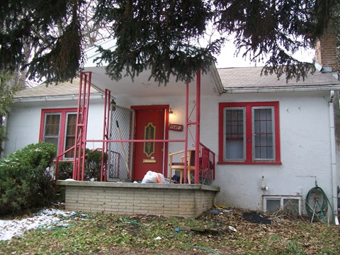 A white house with a red door and red railings.