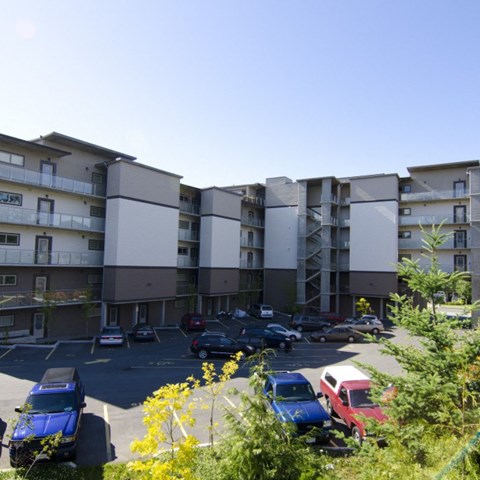 A parking lot in front of a multi-story apartment building with cars parked in it.