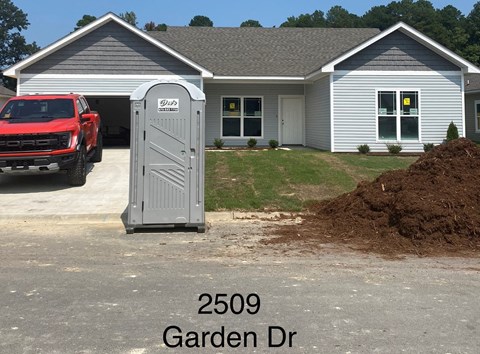 A red truck is parked in front of a house with a porta potty in the driveway.