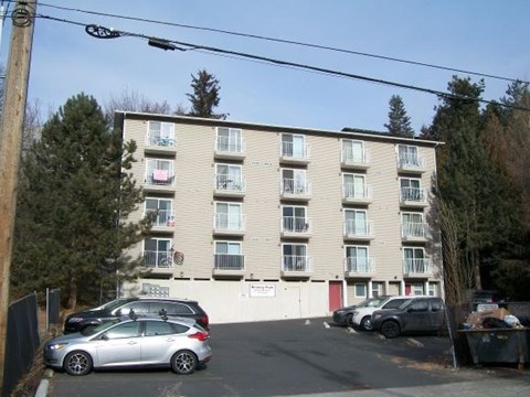 A silver car is parked in front of a building with a white sign on the wall.