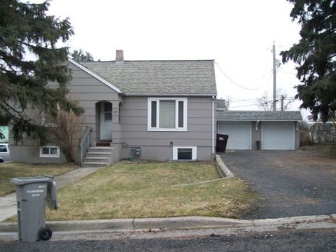 A grey house with a grey trash bin in front of it.