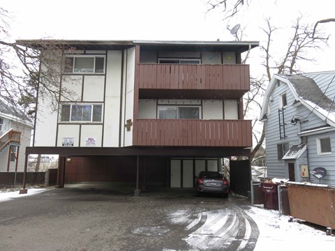A car is parked in the garage of a two-story apartment building.