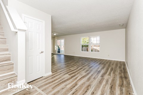 A spacious room with wooden flooring and a staircase on the left side.