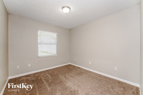 the bedroom of a house with carpet and a window