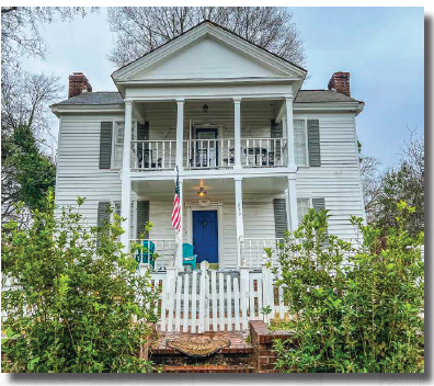 A white house with a blue door and a flag on the porch.