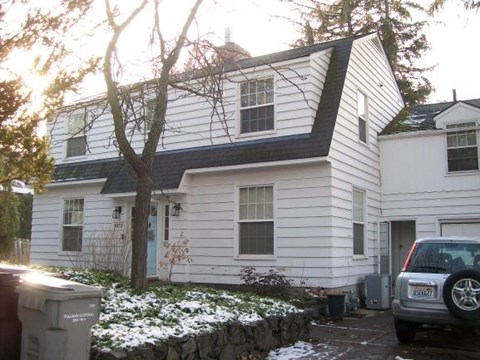 A white house with a grey car parked in front.