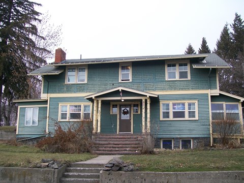 A green house with a front porch and a staircase leading to the front door.