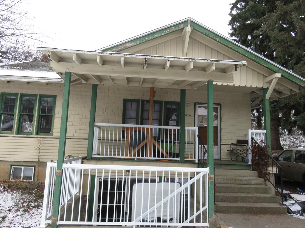 a house with a porch with green posts and a white fence