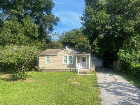A small house with a porch is surrounded by trees.
