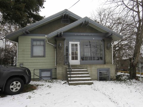 A house with a green siding and a white door is surrounded by snow.