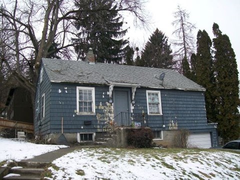 A blue house with a white door and windows is surrounded by snow.