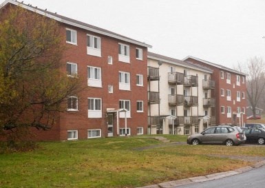 A red brick apartment building with a green lawn in front.