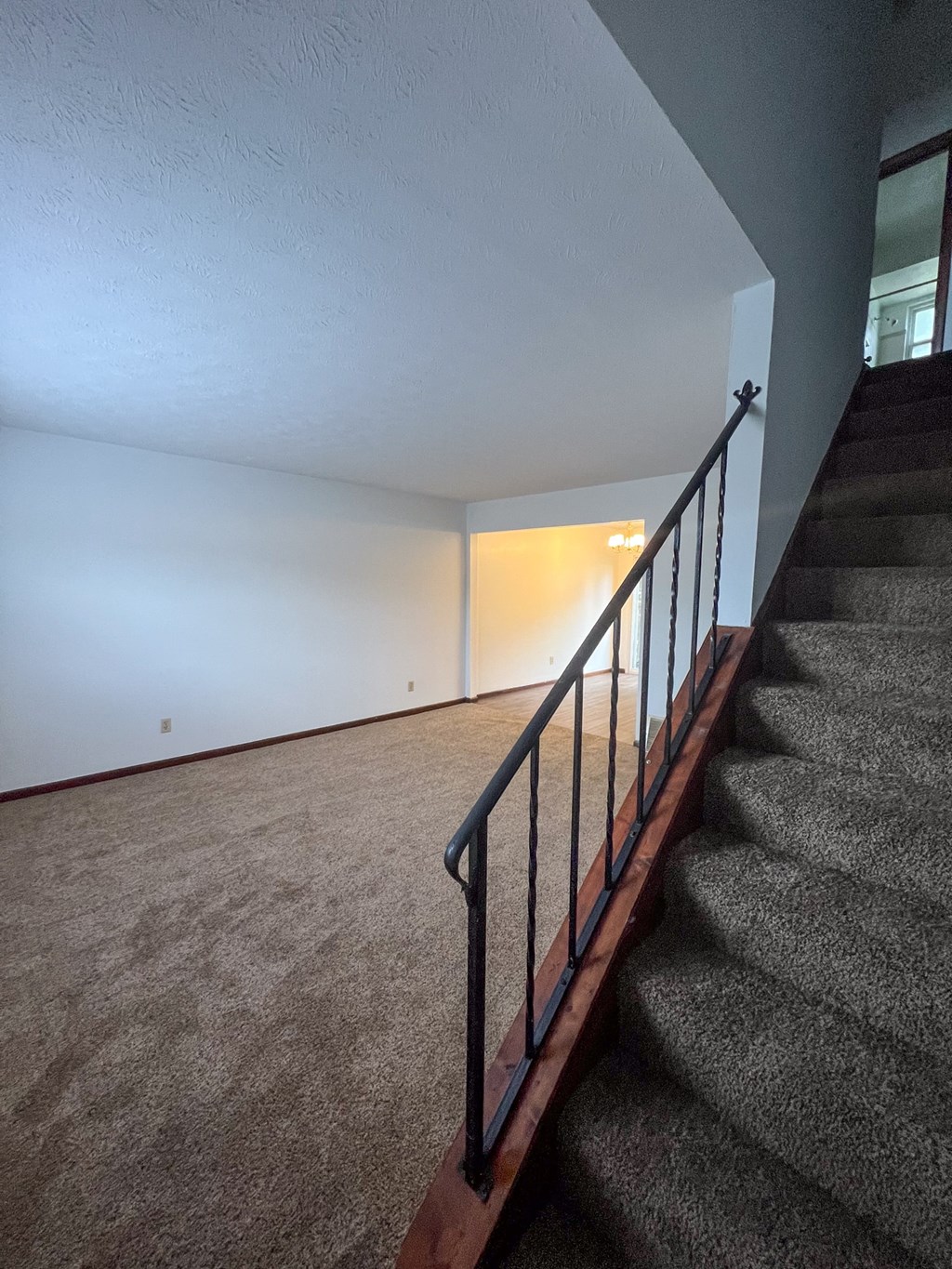 the upstairs living room with carpeted stairs and a railing