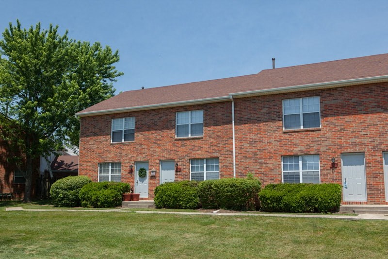 the front of a brick house with a lawn and a tree