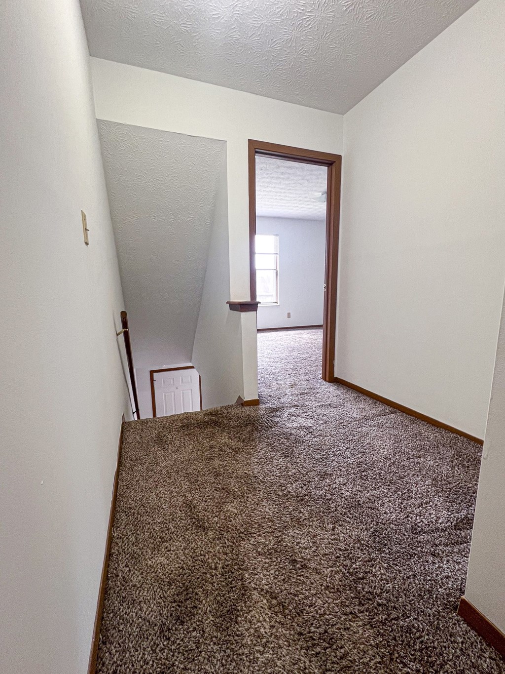 an empty hallway with a carpeted floor and a door to a bedroom