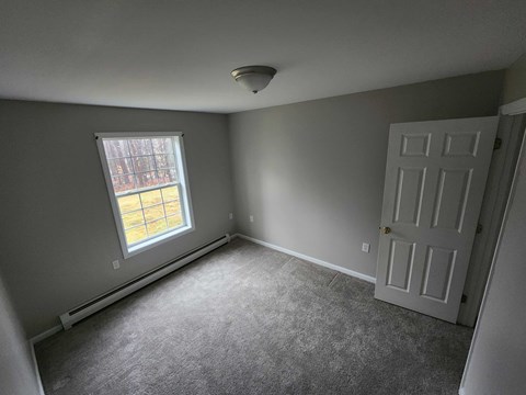 A room with a carpeted floor, a white door, and a window with a view of a building outside.