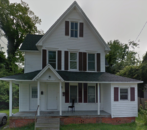 A white house with a black roof and a red brick base.