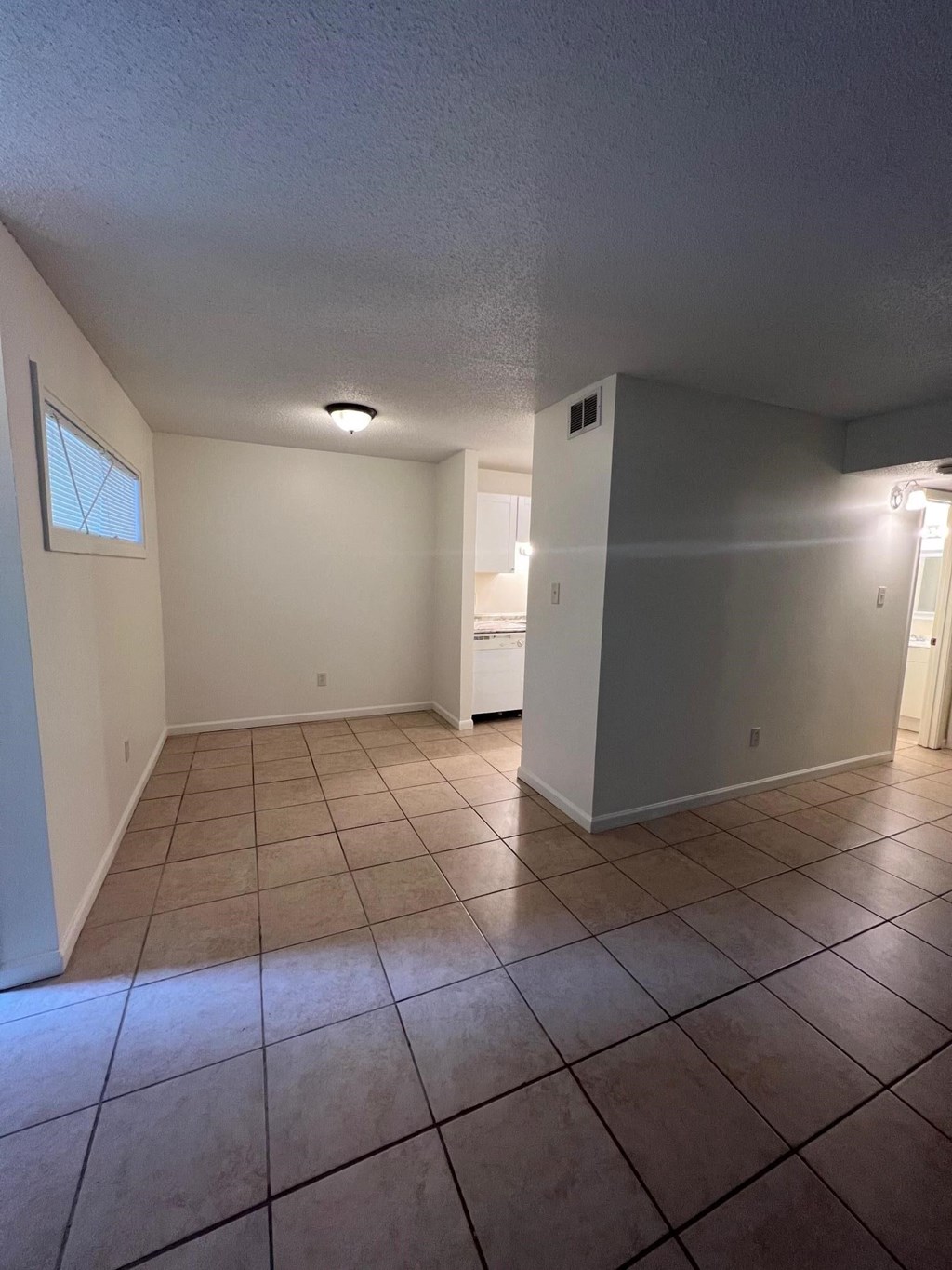 an empty living room with tiled floors and a kitchen