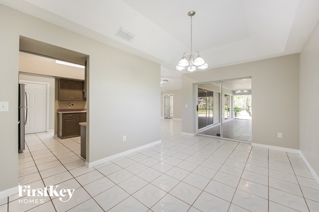 A spacious room with a white tile floor and a chandelier hanging from the ceiling.