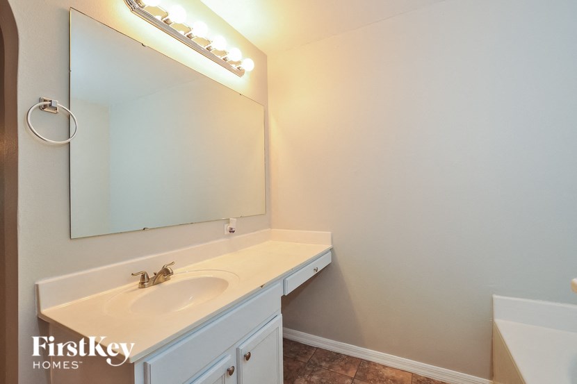 A bathroom with a white sink and a mirror with lights on it.
