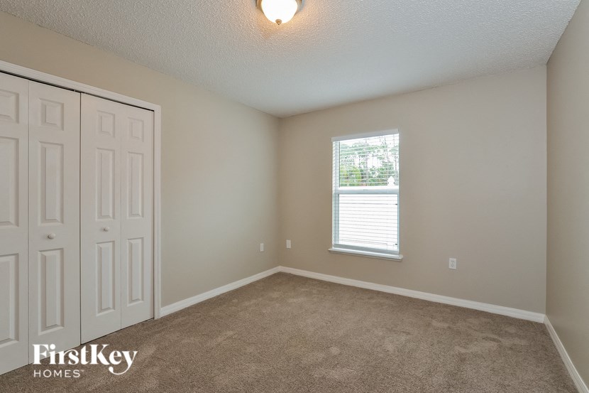A room with a carpeted floor, a window with blinds, and a white door.