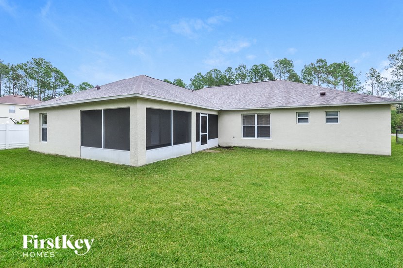A house with a white exterior and a brown roof is surrounded by a grassy lawn.