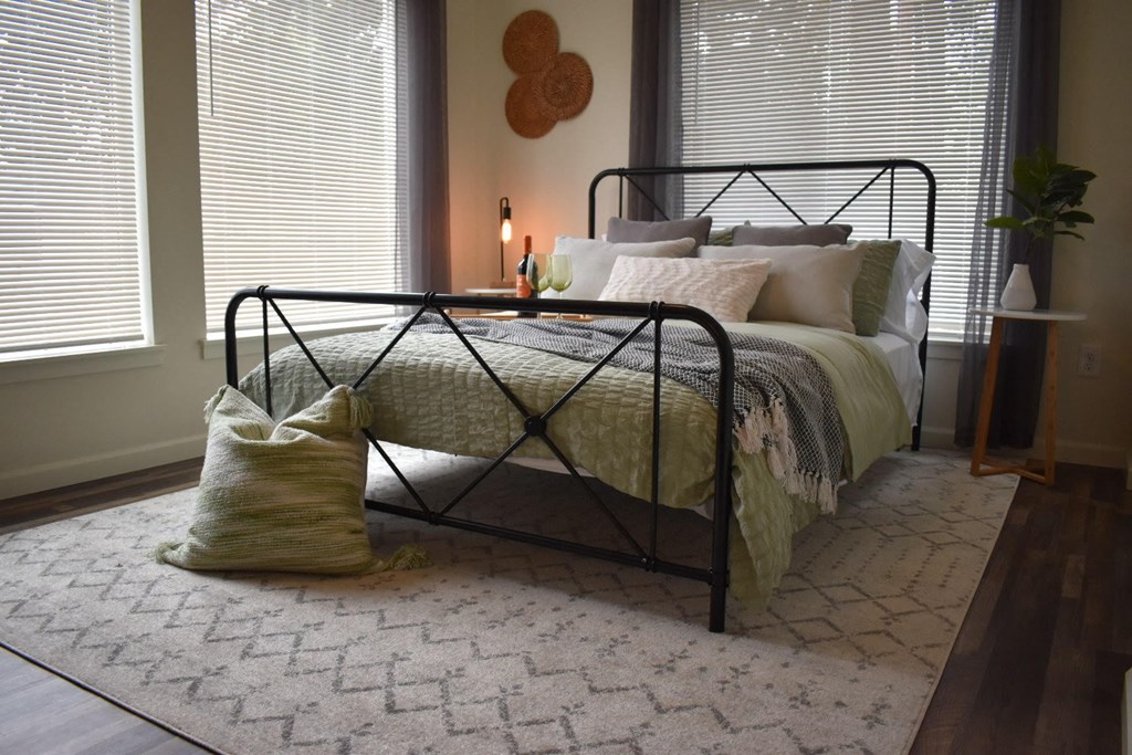 a bedroom with a bed and a rug and two windows