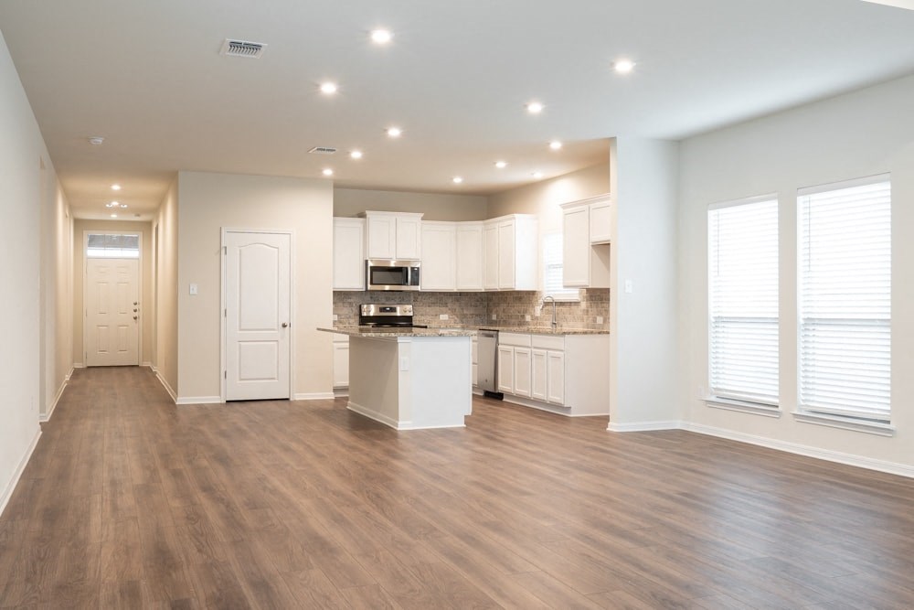 an empty living room with a kitchen with white cabinets